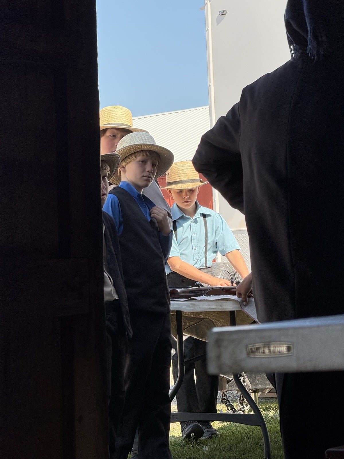 Amish boys in straw hats clustered around table closely inspecting an item at Gladwin County Michigan auction