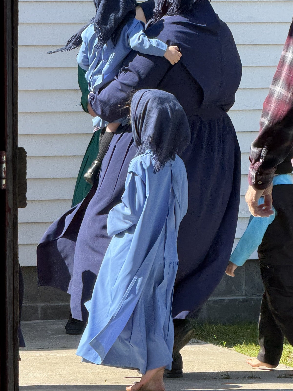 Amish women and girls in dark dresses and head coverings walking at auction grounds barefoot girl visible