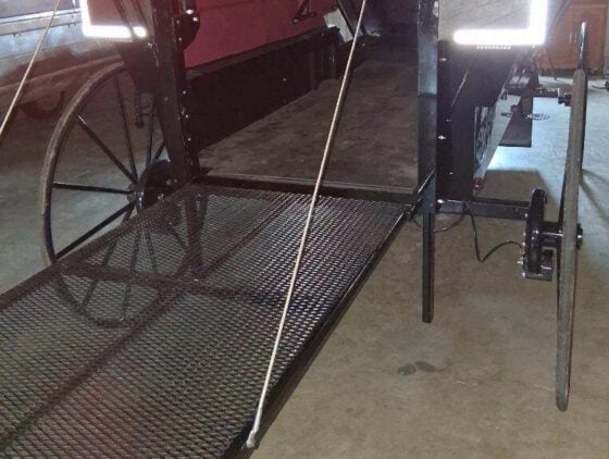 Vintage wagon with a metal mesh loading ramp, large spoked wheels, and a hitch, positioned indoors.