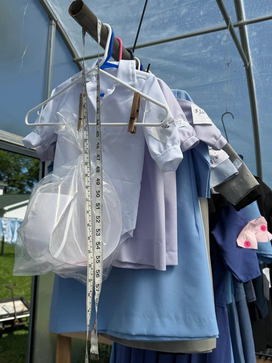 Amish dresses on hangers with a tape measure and handwritten price tags at a Michigan sale
