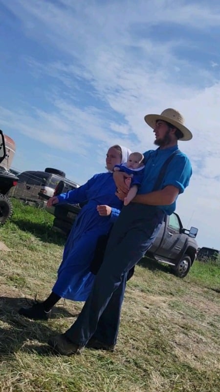 An Amish family walking through the auction parking lot, father carrying a baby