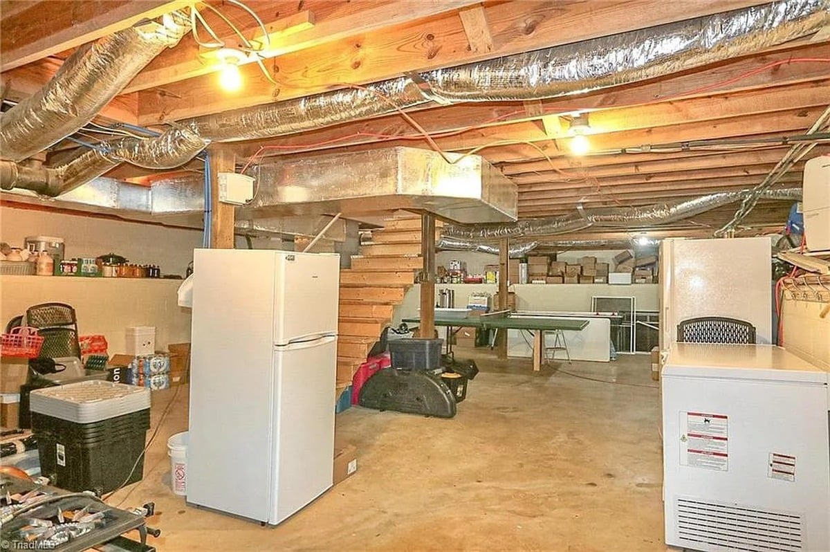 Unfinished basement of Amish home in Hamptonville, NC with refrigerator, chest freezer, ping pong table, and exposed ductwork