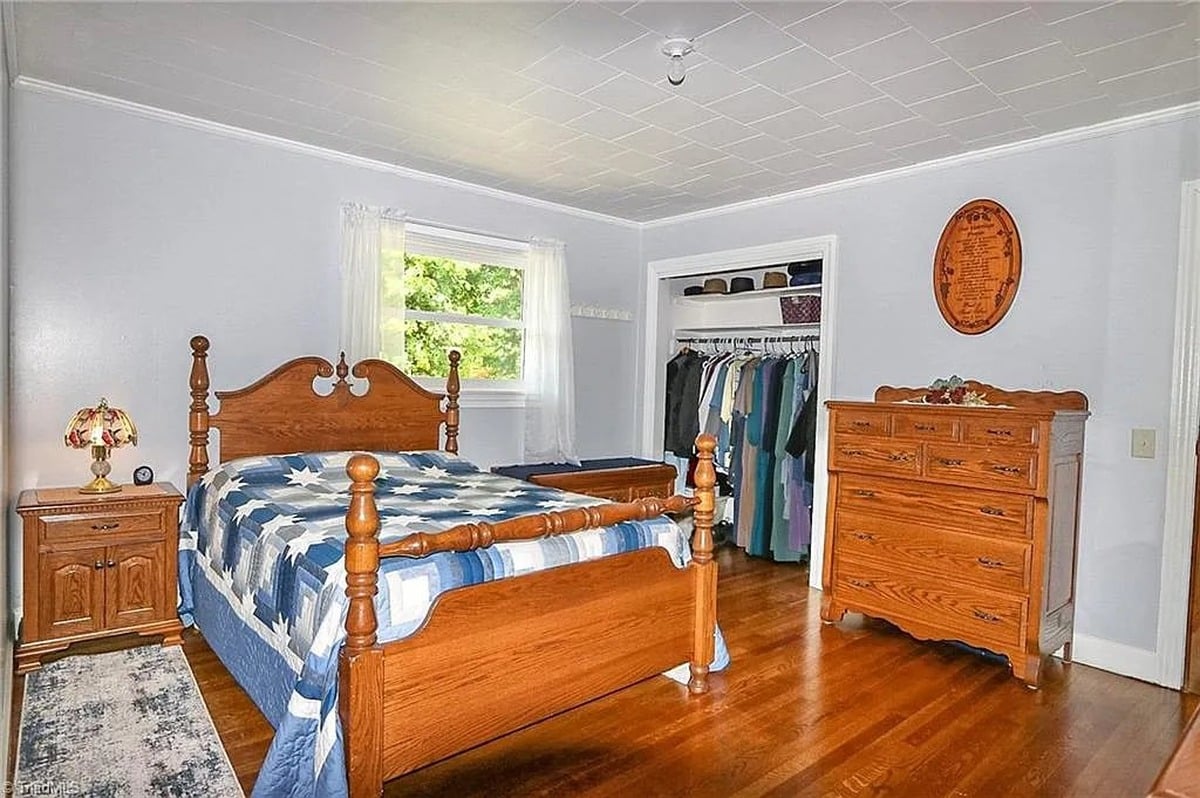 Primary bedroom of Amish home in Hamptonville, NC with four-poster bed, blue star quilt, and plain Amish clothing in open closet