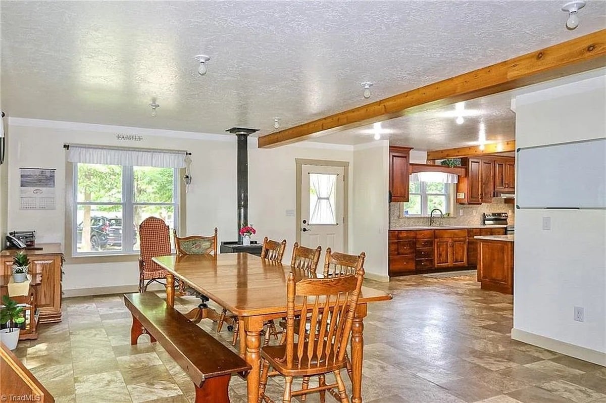 Dining room of Amish home in Hamptonville, NC with long farm table, bare ceiling light bulbs, and view into main kitchen