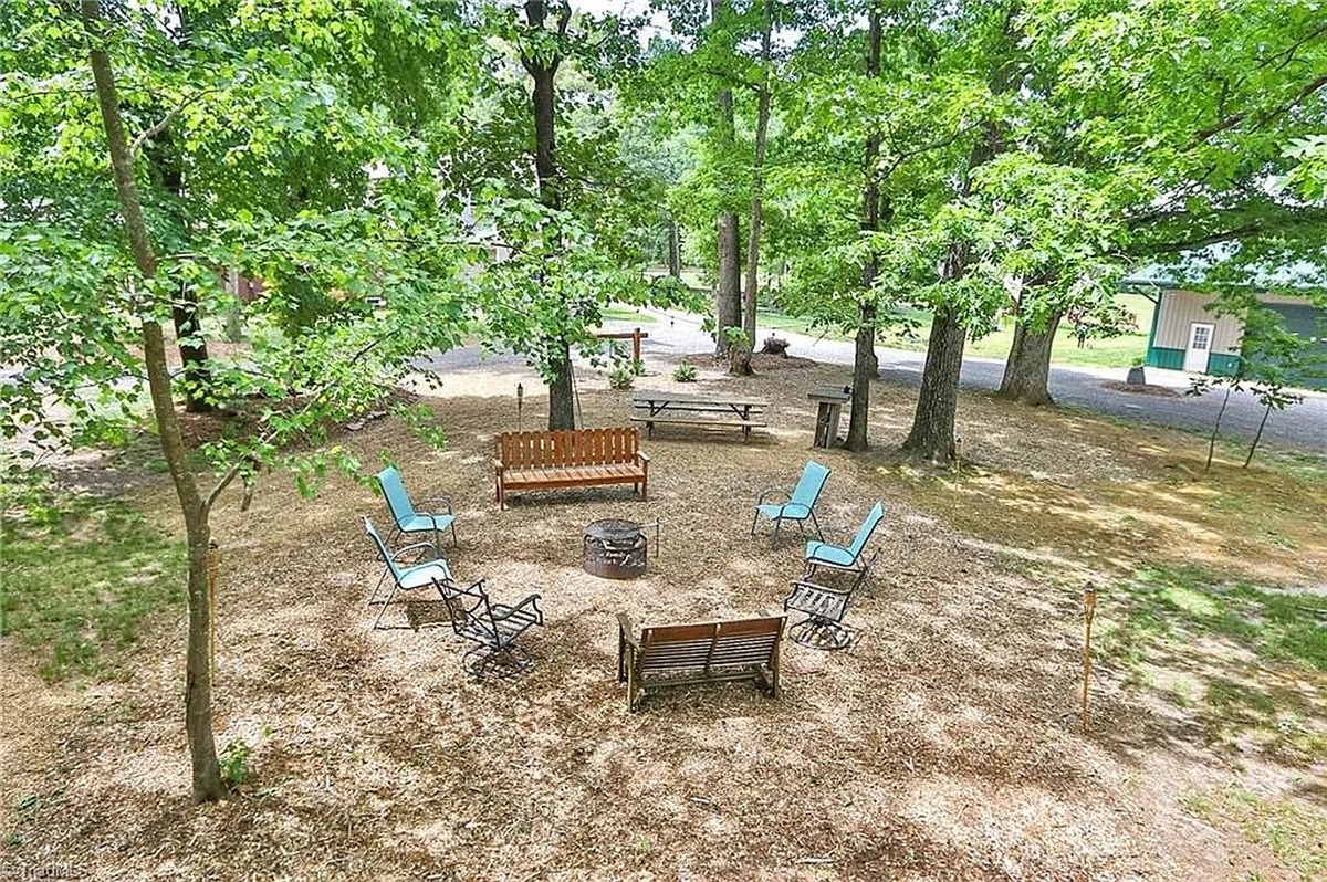 Fire pit seating area with wooden bench and chairs under trees at Amish property in Hamptonville, North Carolina