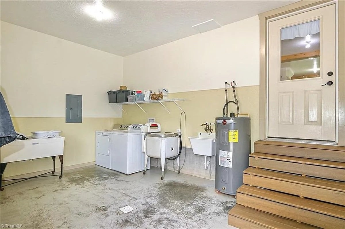 Laundry room with washer, dryer, utility sink, water heater, and wooden steps in Amish home, Hamptonville, NC
