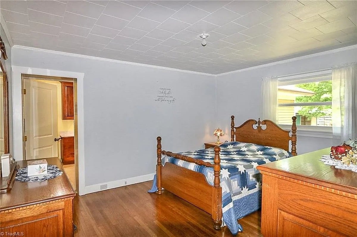 Primary bedroom of Amish home in Hamptonville, NC showing four-poster bed with blue star quilt from second angle with ensuite bathroom doorway visible