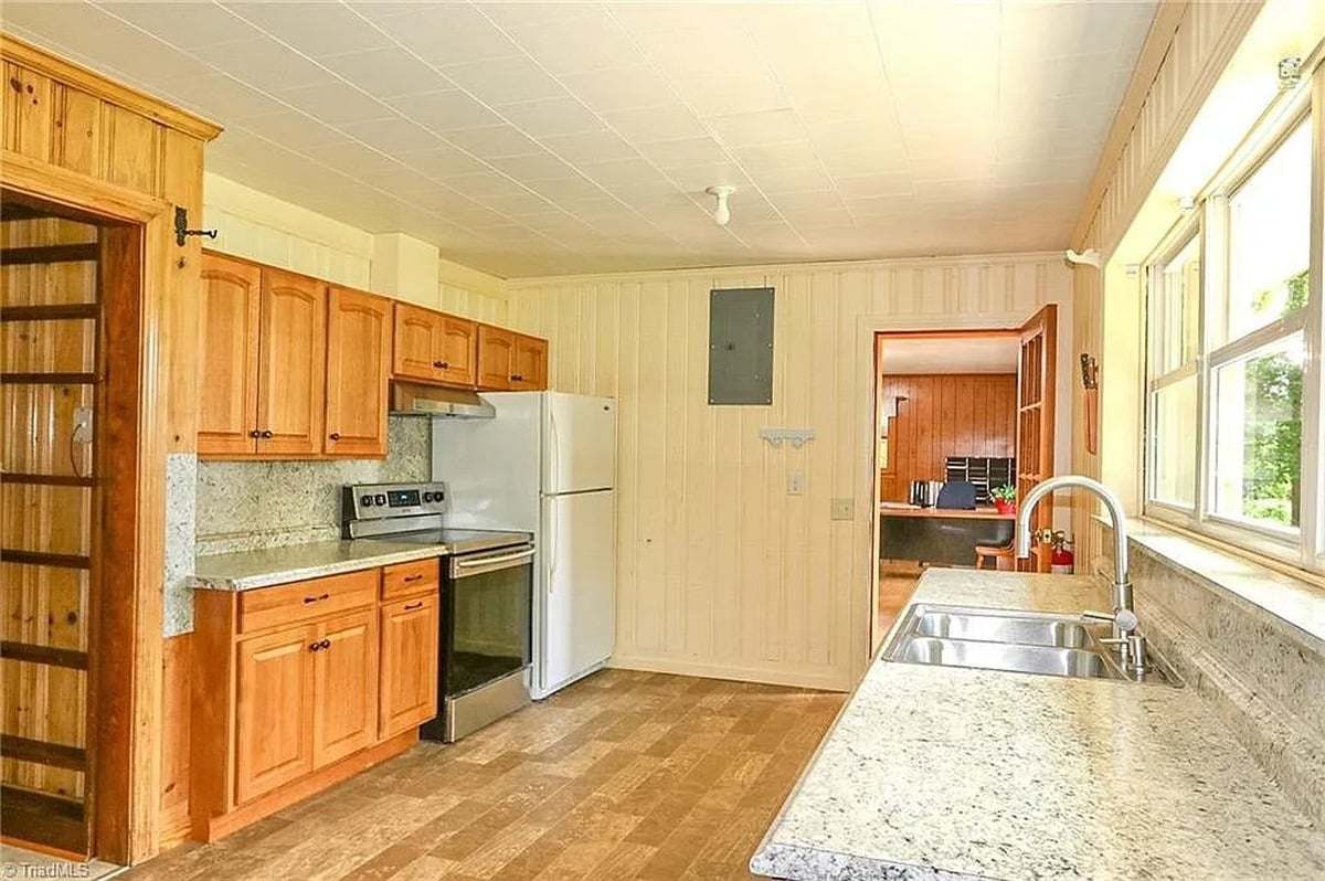 Second kitchen in original section of Amish home in Hamptonville, NC with lighter wood cabinets, wood-paneled walls, and single bare ceiling bulb
