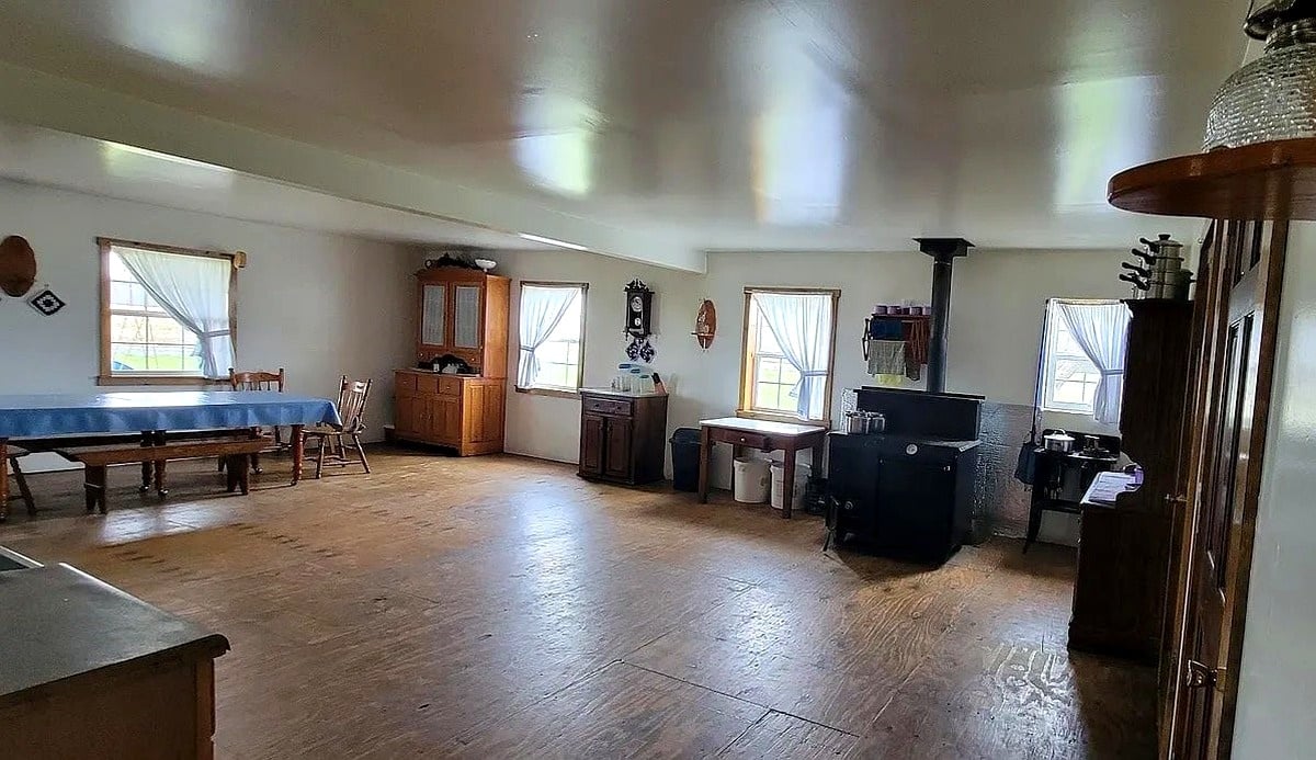 Wide view of main living area inside Amish home in Vevay, Indiana with wood stove, dining table, and hardwood floors