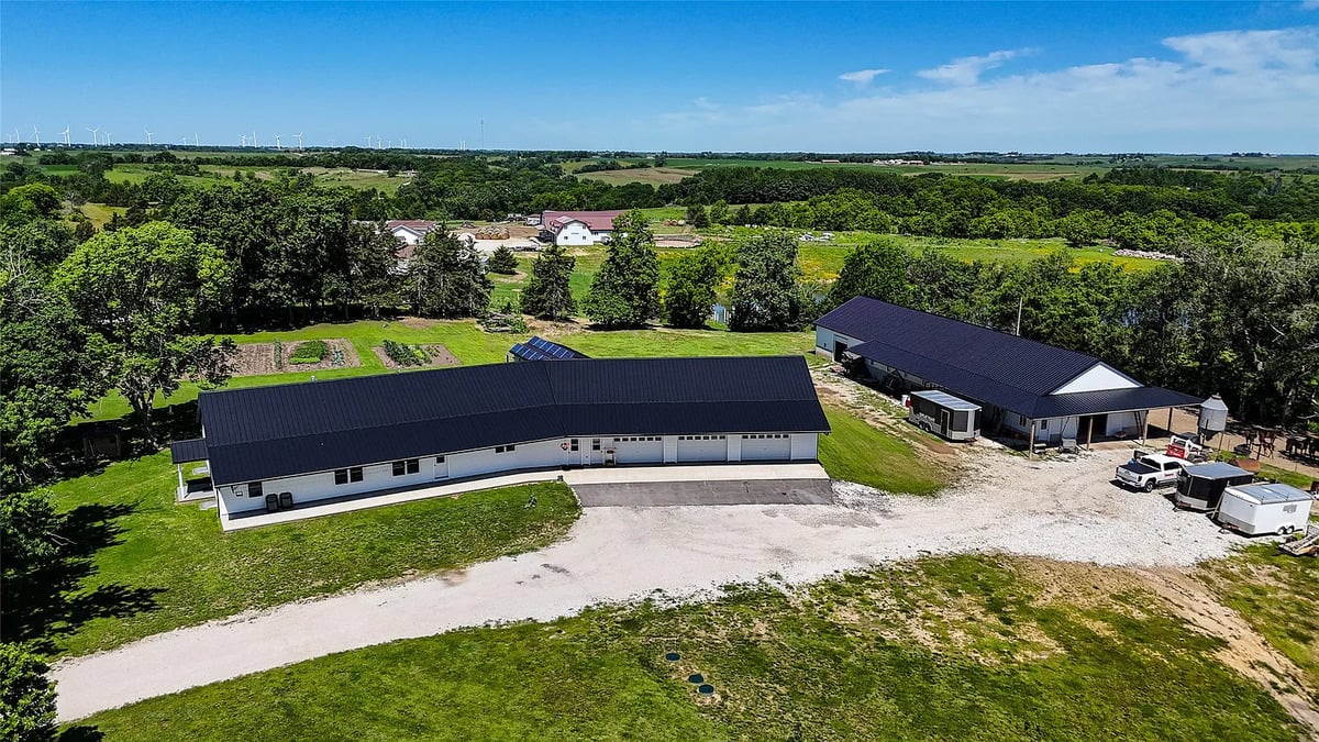Aerial view of the long Winterset Amish home with solar panels and shop Aerial view of long Amish ranch home with solar panels and large steel shop building, wind turbines on horizon