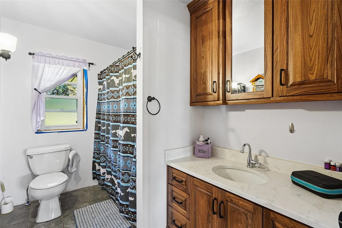 Bathroom with wood vanity in the Winterset Amish home Amish bathroom with wood vanity, marble-look countertop, and horse-print shower curtain