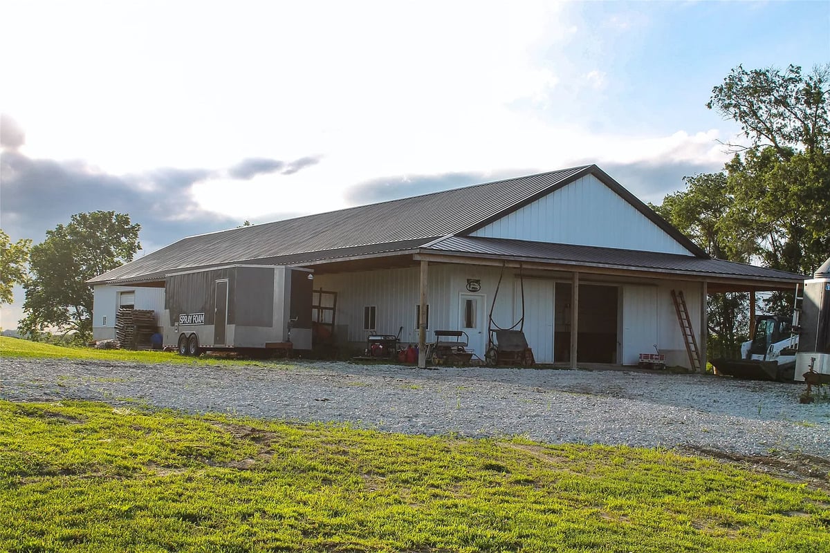 Steel shop building with Spray Foam trailer at the Winterset Amish homestead Large steel Amish shop building with an enclosed Spray Foam trailer and skid steer parked outside