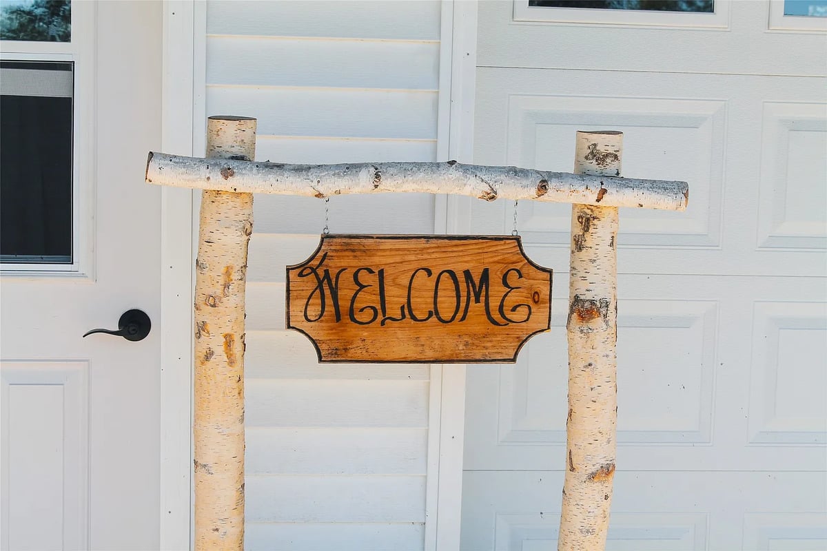 Hand-lettered birch-log Welcome sign at the Winterset Amish home Hand-lettered wooden Welcome sign hung between two birch posts at an Amish home