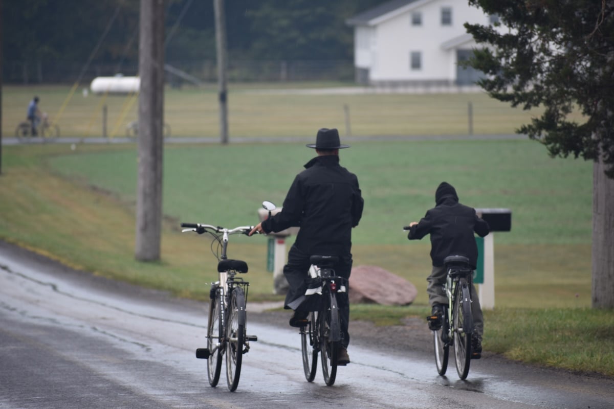 Amish man and child riding bicycles on a rural road in the rain