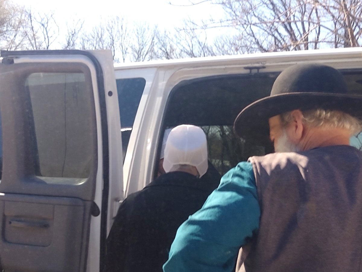 Amish man in broad-brimmed hat and Amish woman boarding a white passenger van