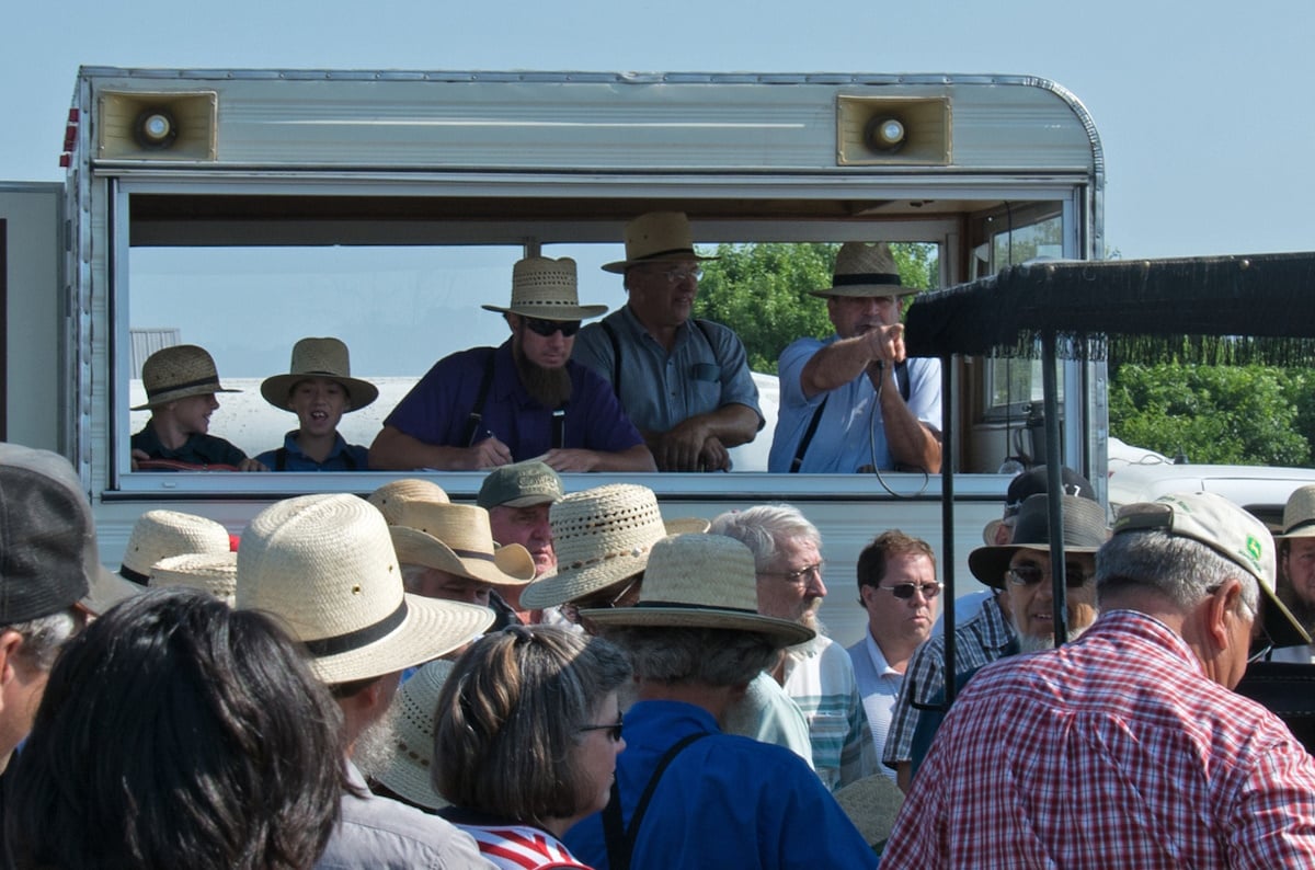 Crowd of Amish and non-Amish at an Amish school auction, with auctioneers calling from a raised booth
