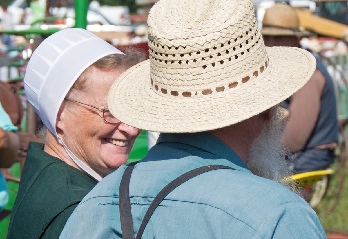 Amish woman smiling warmly at an Amish man in a straw hat at an outdoor gathering