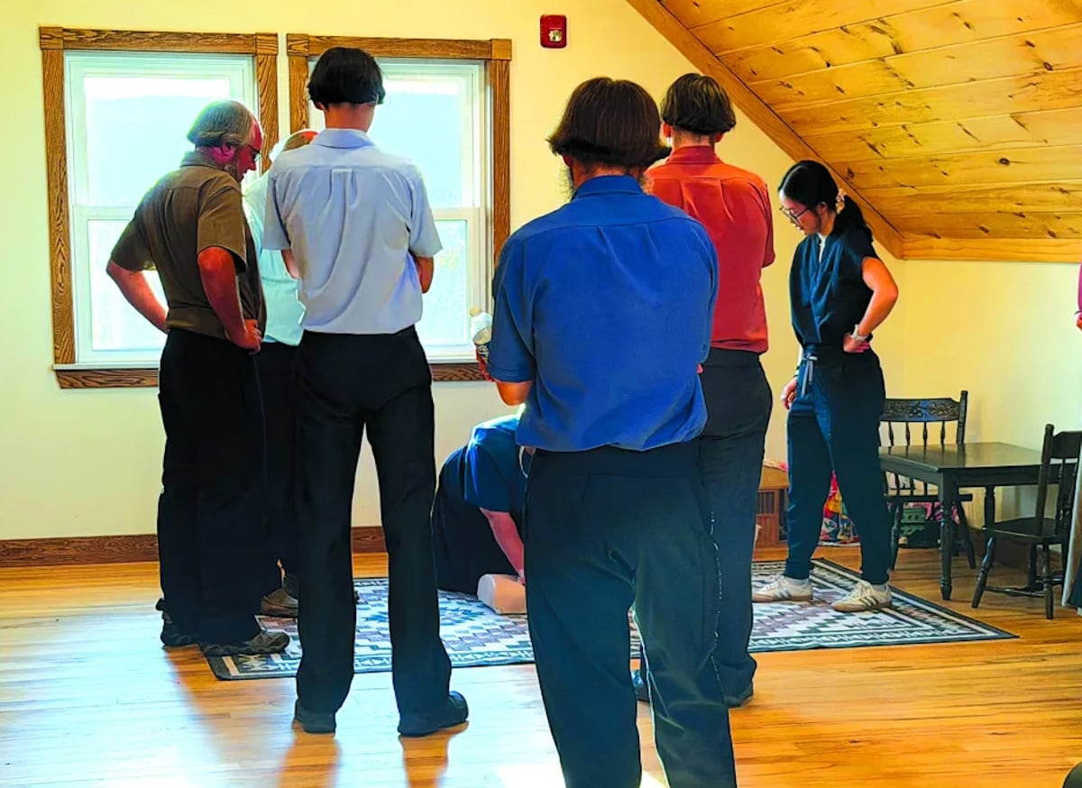 An Amish woman practices CPR techniques on a training device as Amish men and a trainer observe