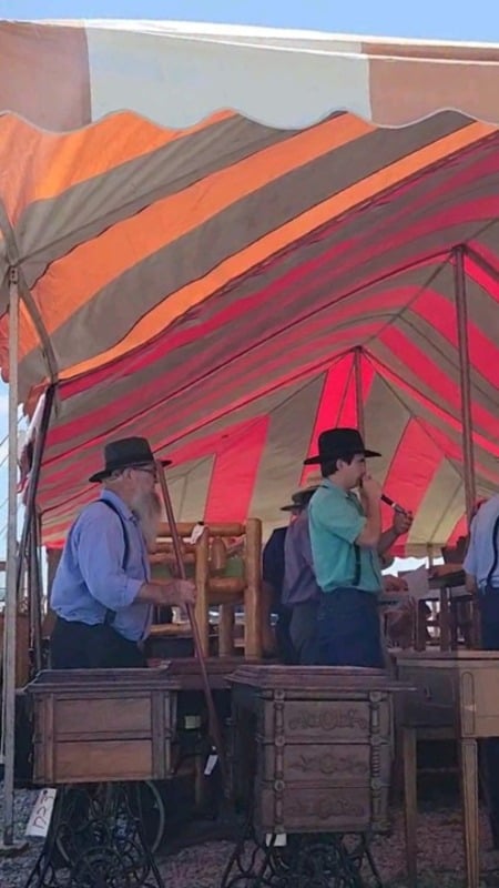 An auctioneer calling bids on furniture under a striped auction tent