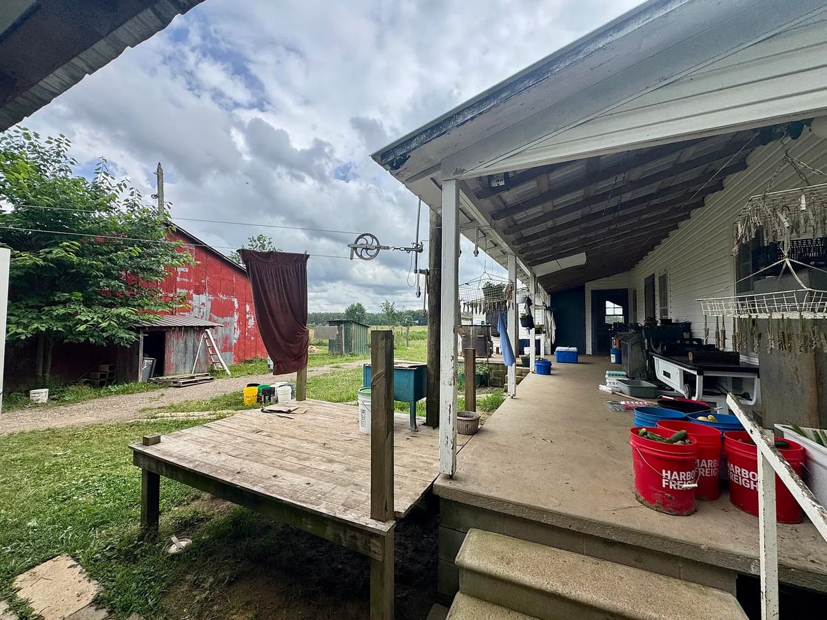 Covered back porch with buckets of cucumbers and pulley clothesline at an Amish home in Randolph, Mississippi