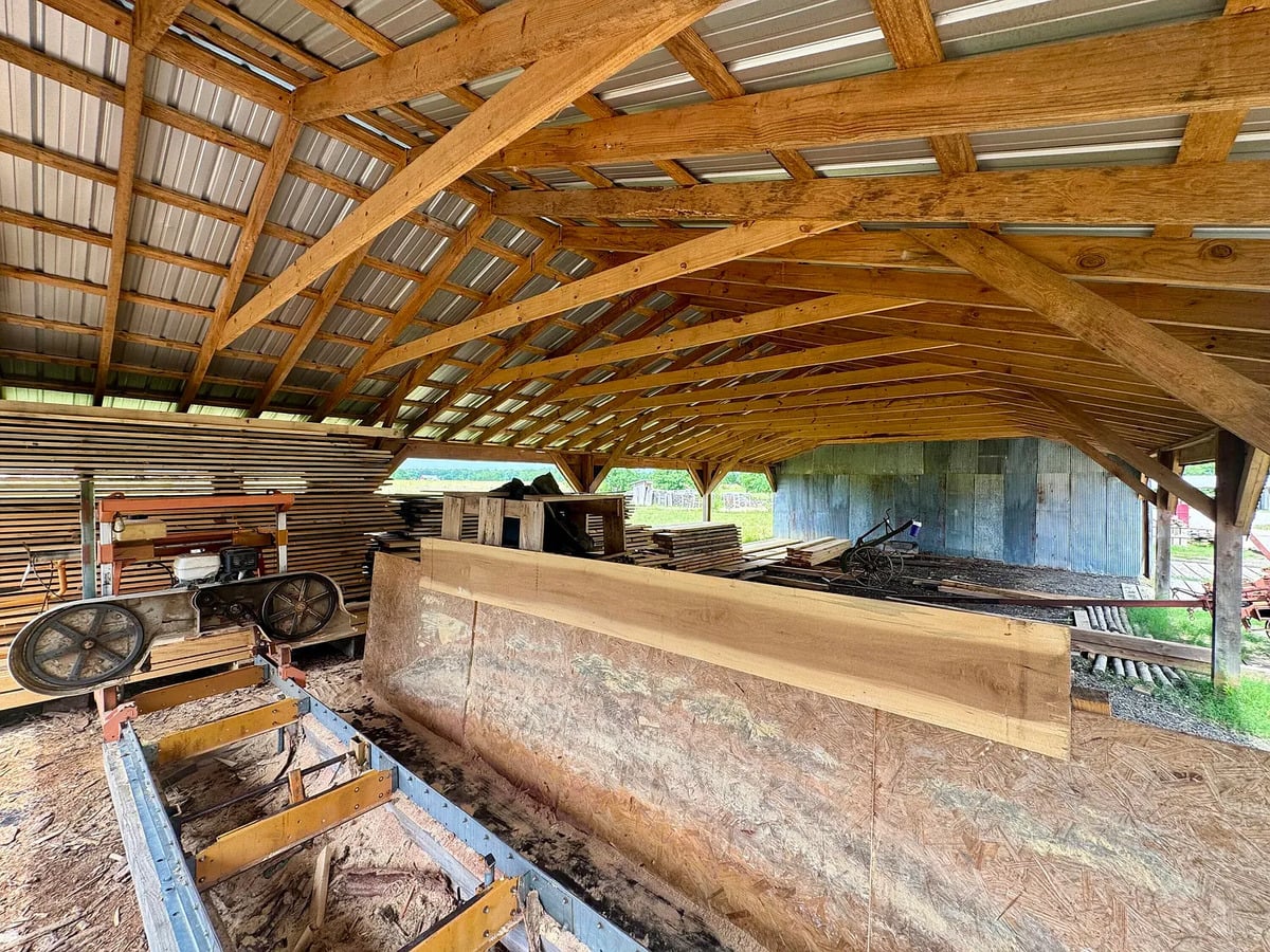 Band sawmill and stacked lumber under timber-framed pole shed, Amish farm in Mississippi