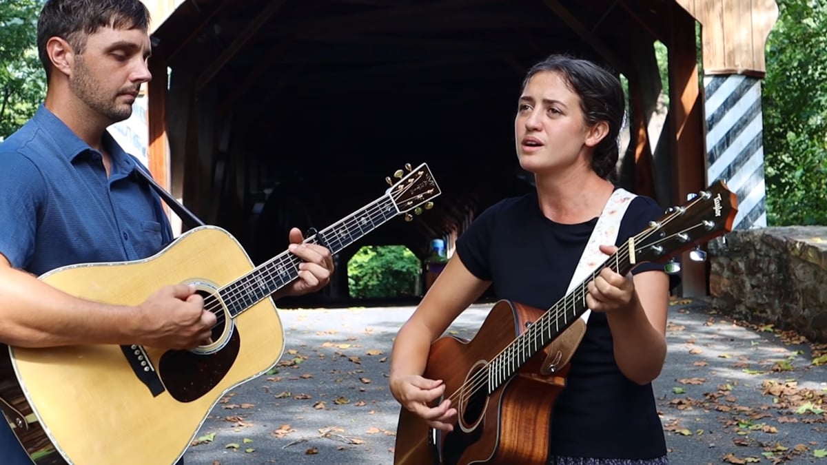 Ben and Rose in front of a covered bridge in the Will You Travel Down This Road With Me video
