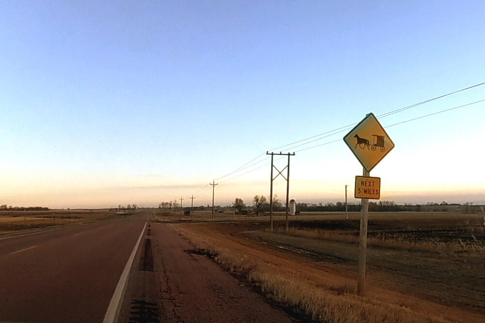 Amish buggy warning sign on a long highway at dawn