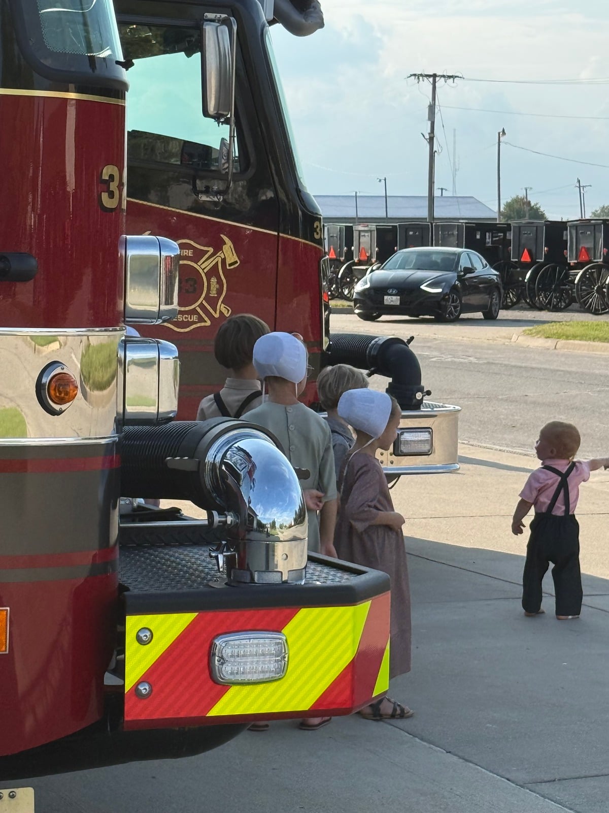 Amish children at the front of a fire engine with buggies parked in the background