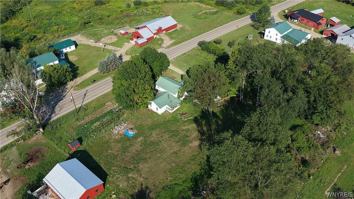Wide aerial view showing neighboring Amish farms with green metal roofs and red barns along Route 241