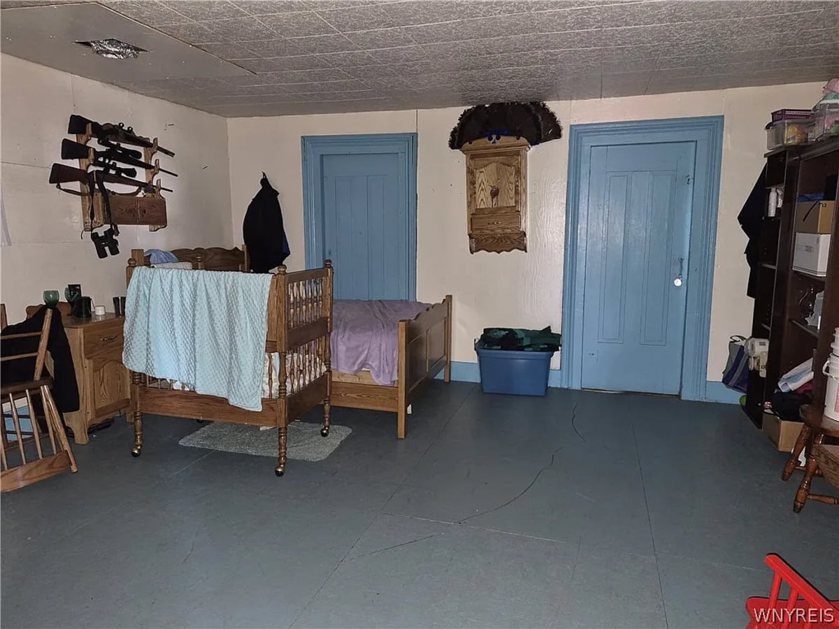 Amish bedroom with a wooden cradle on casters, a single bed, and three long guns on a wall rack