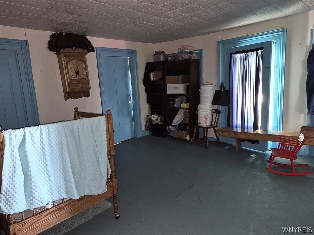 The same Amish bedroom from the opposite side, with shelving, five-gallon buckets, and a small red rocking chair