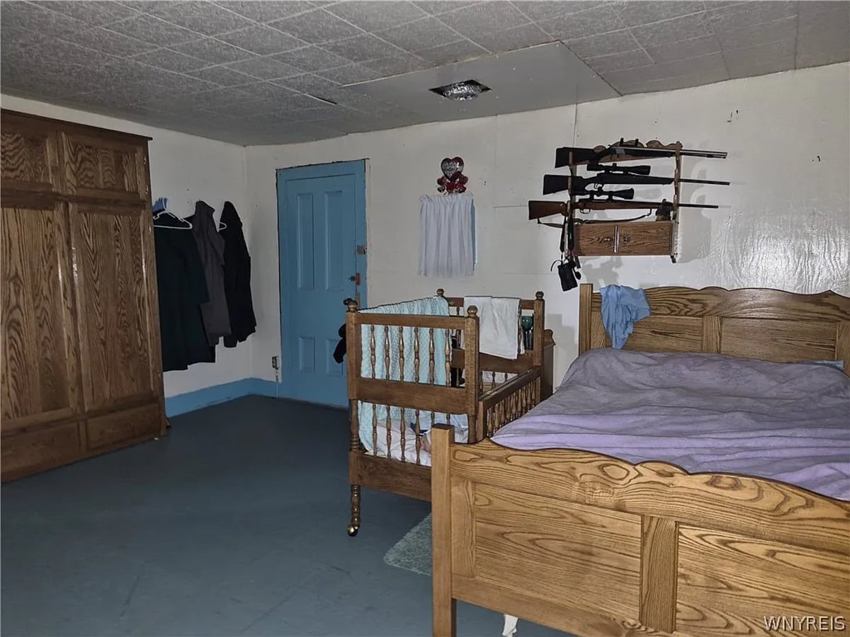 Amish bedroom with a large oak wardrobe, dark coats and a child's blue dress hanging on wall pegs