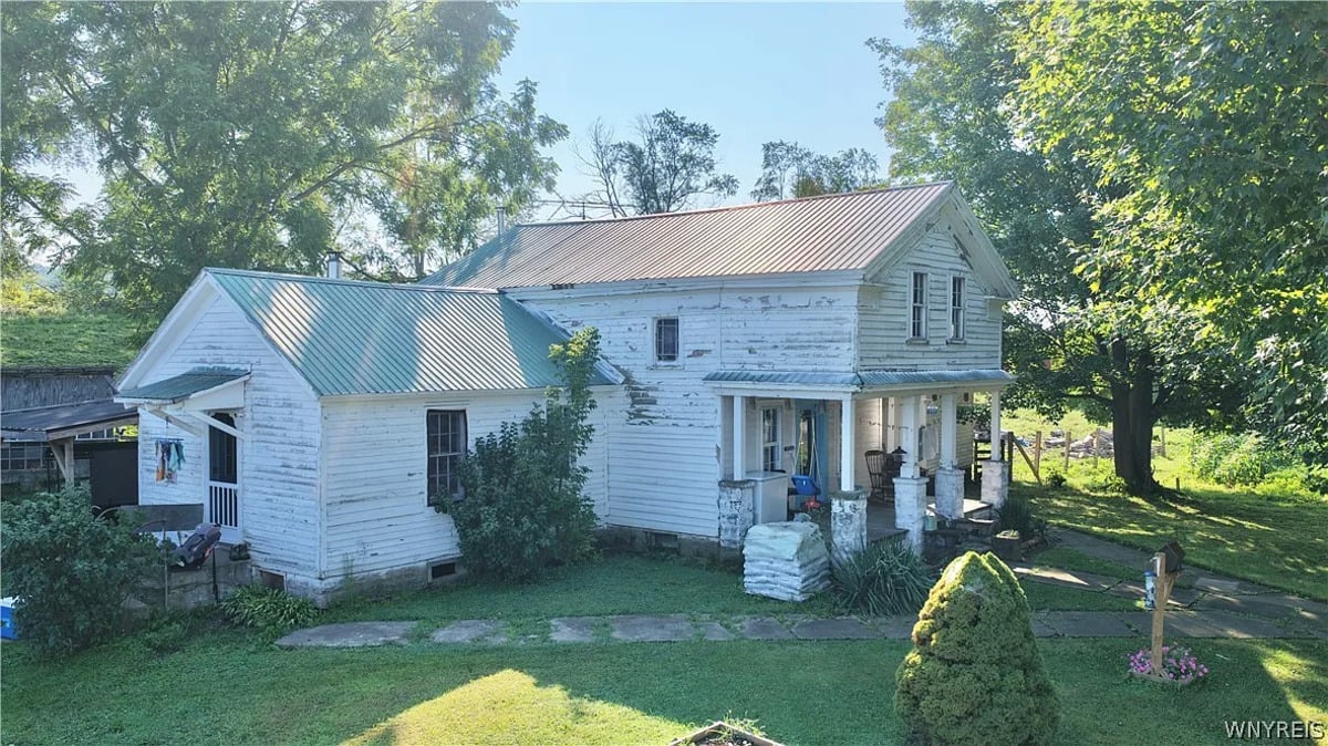 White clapboard Amish farmhouse with peeling paint and a two-tone metal roof in Conewango Valley, New York