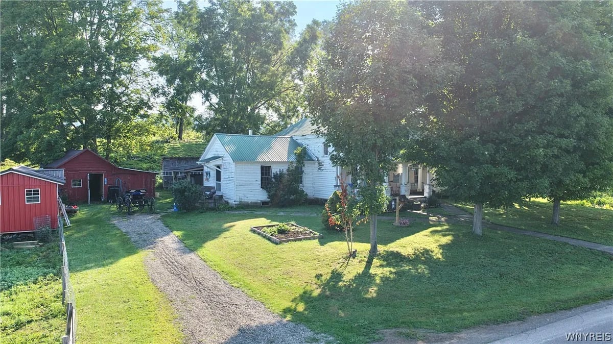 Amish home seen from Route 241 with a mown lawn, garden bed, and red outbuildings behind