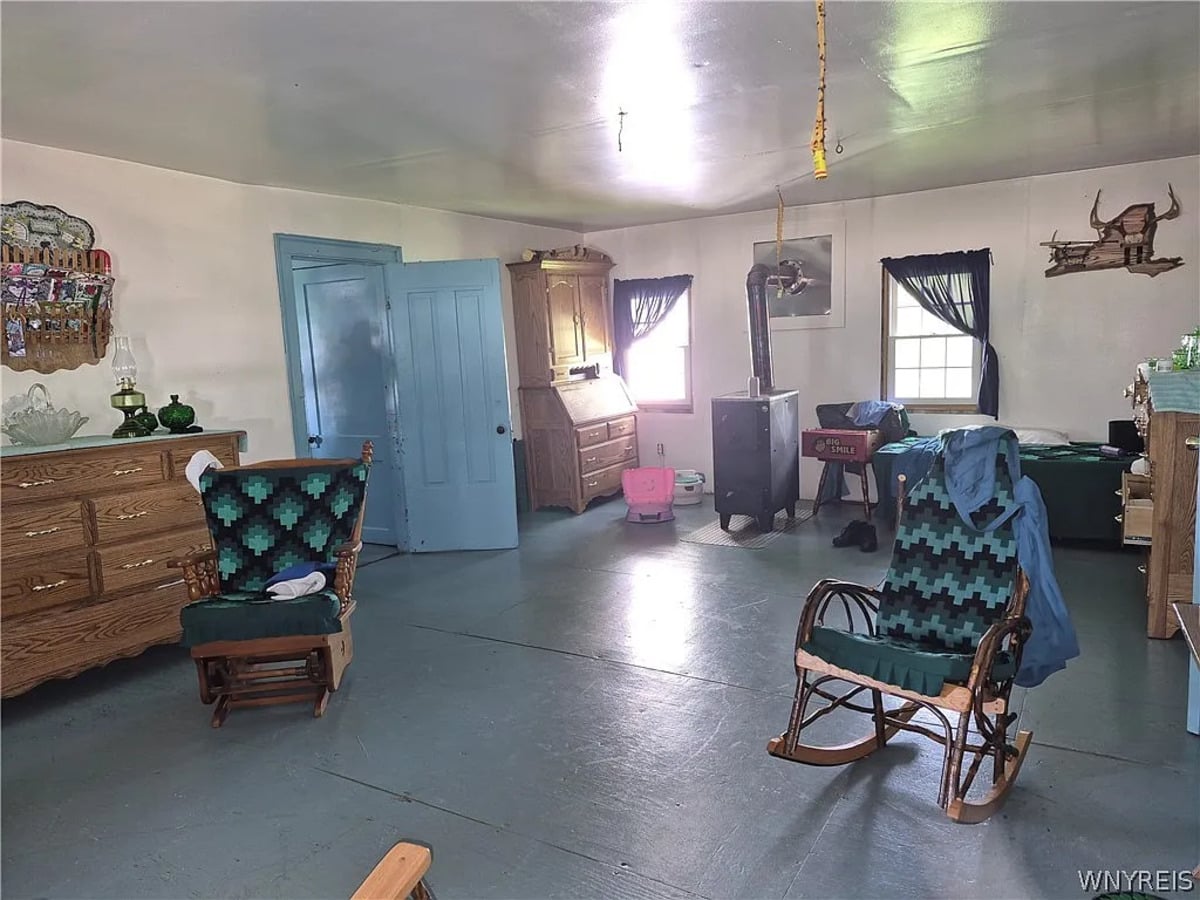 Amish front room with a bed, oak secretary desk, oil lamps on a shelf, and a bare ceiling hook