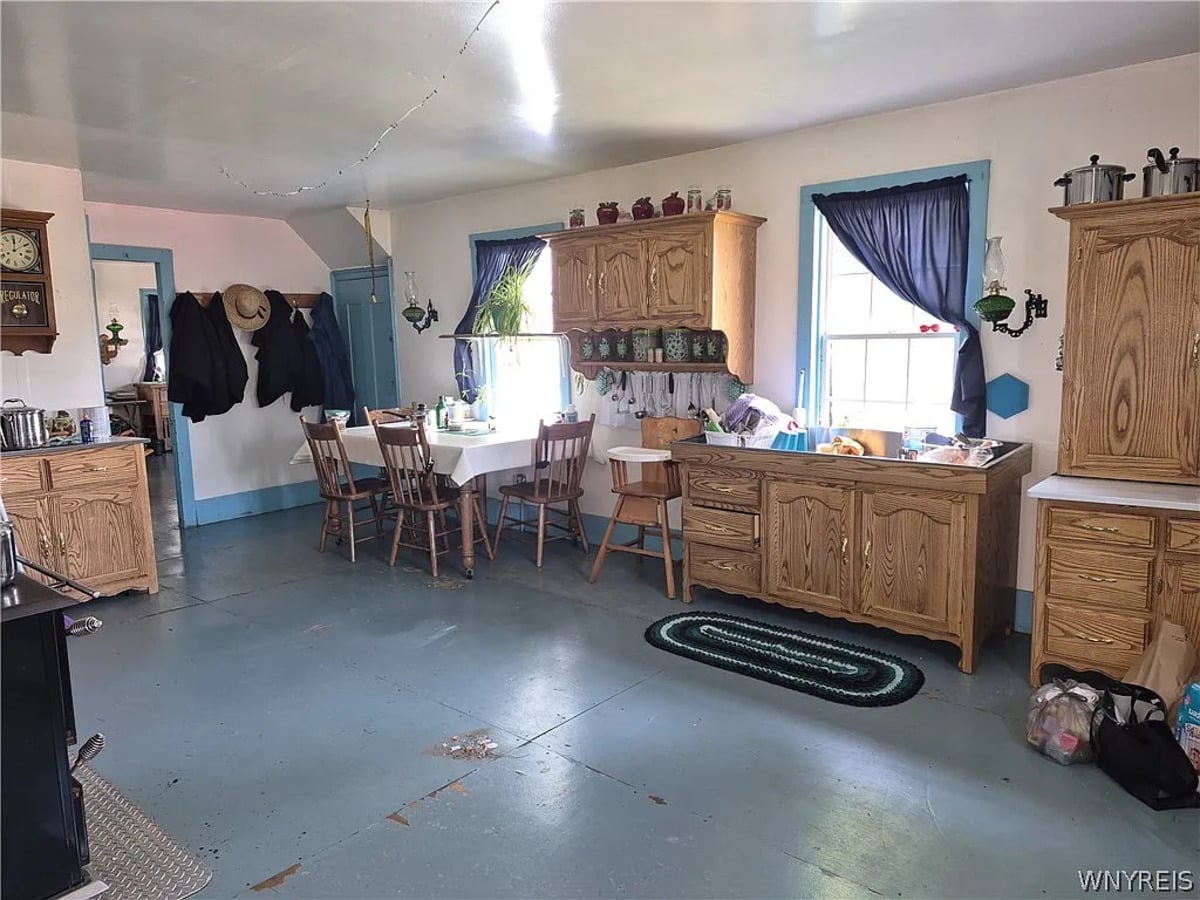 Dark coats and a straw hat hanging on kitchen wall pegs beside a high chair and braided rug