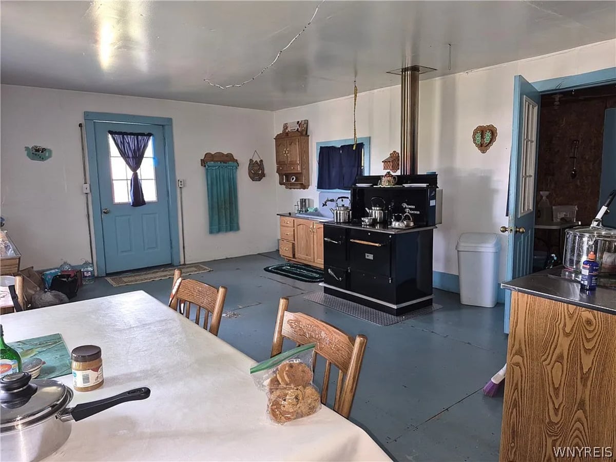 Black enameled wood cookstove with kettles on top and a stovepipe running to the ceiling in an Amish kitchen