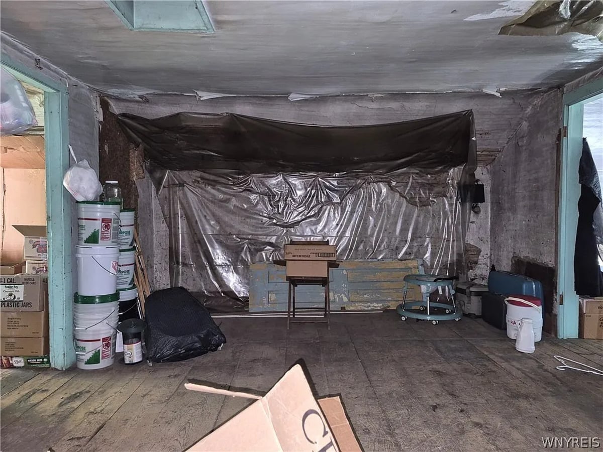 Low-ceilinged room with heavy plastic sheeting tacked over a stone wall and buckets stacked along the side