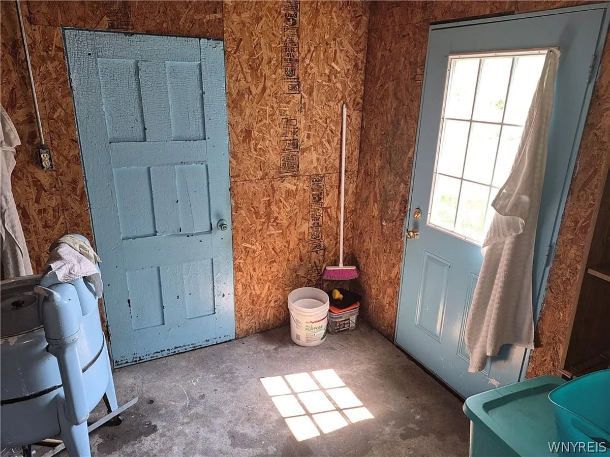 Interior of the Amish wash house with OSB walls, a concrete floor, blue doors, and a green tub in the corner