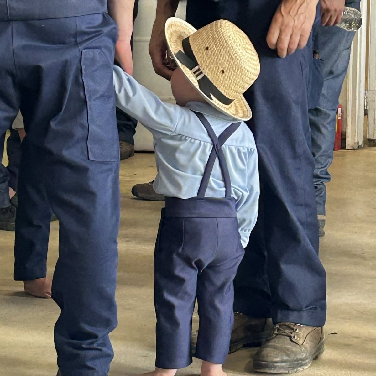 A small Amish boy in a straw hat standing among adults at the DDC Clinic benefit auction