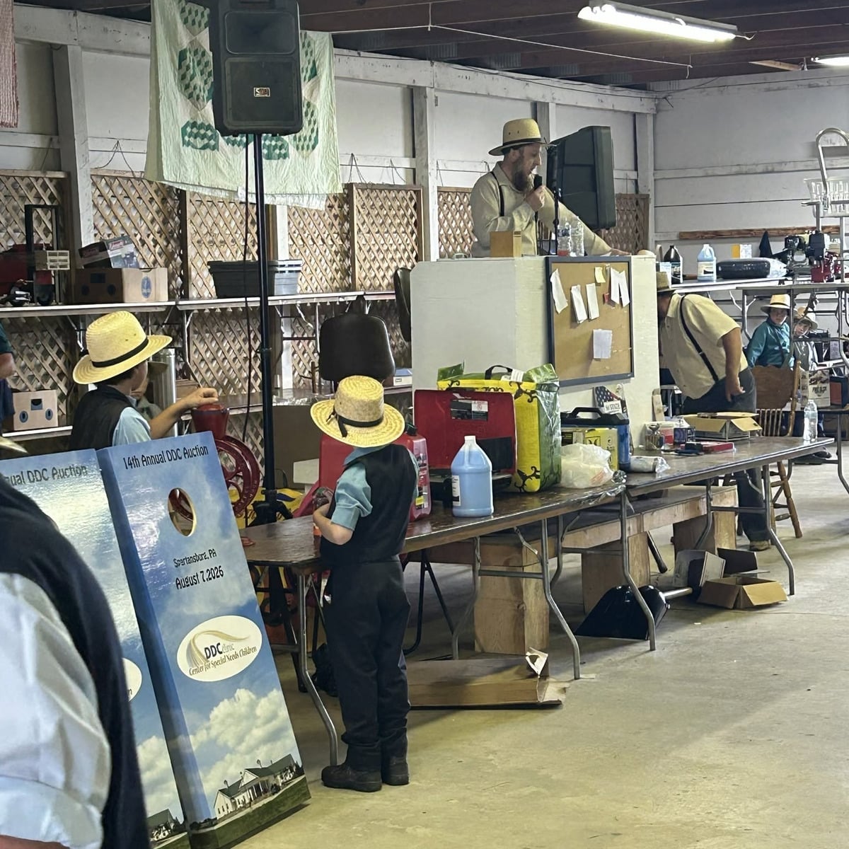 An Amish auctioneer at the microphone with items lined up on a table at the DDC Clinic benefit auction