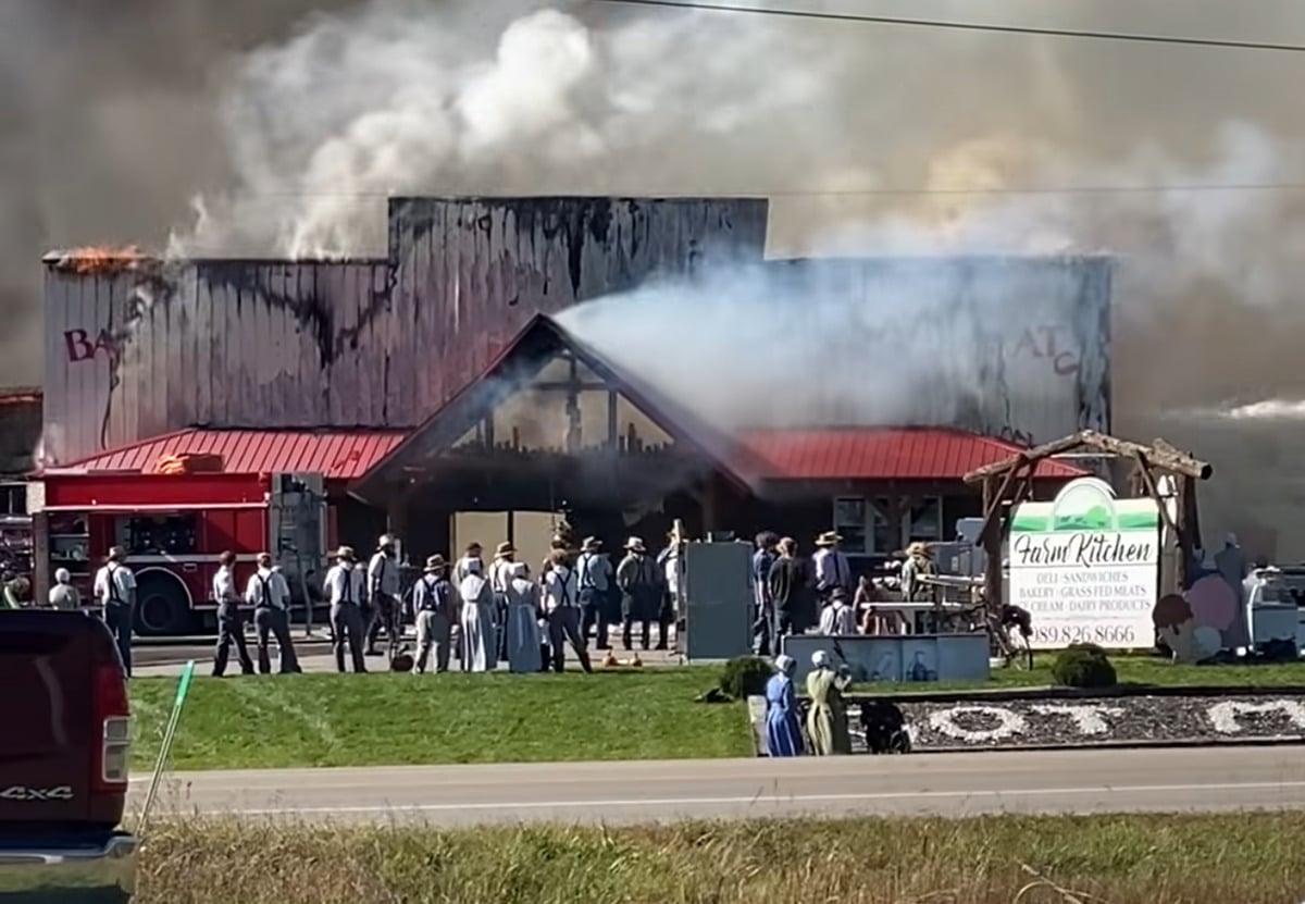 Smoke and flames rise from The Farmers' Creamery as Amish community members and a fire truck stand outside the Farm Kitchen store in Mio, Michigan