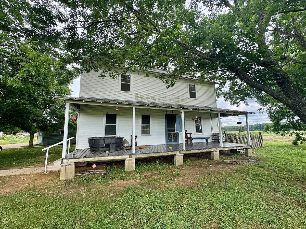 White two-story Amish farmhouse with covered front porch under large shade trees, Randolph Mississippi