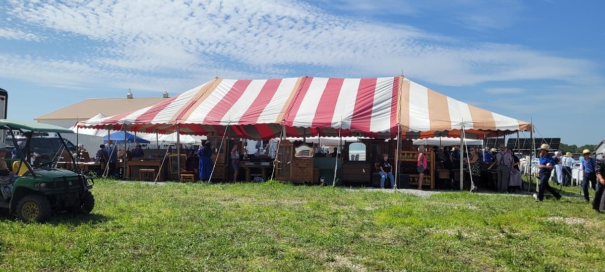 Red and white striped tent sheltering rows of used furniture at the auction