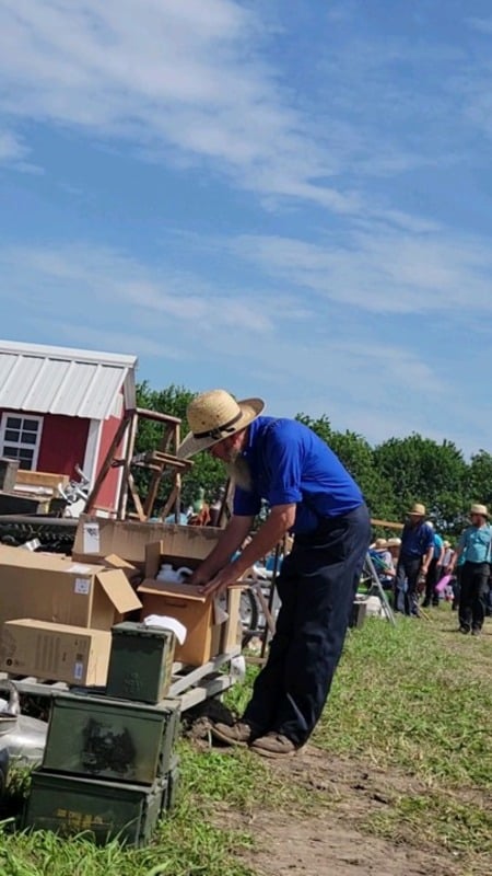 An Amish man leaning over to look through a cardboard box of auction items