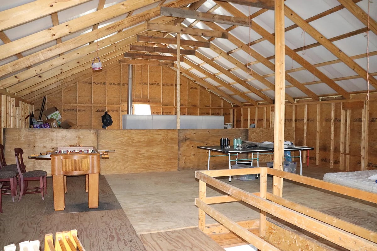 Wide view of the unfinished upstairs of an Amish home with bare studs, plywood floor, and exposed rafters