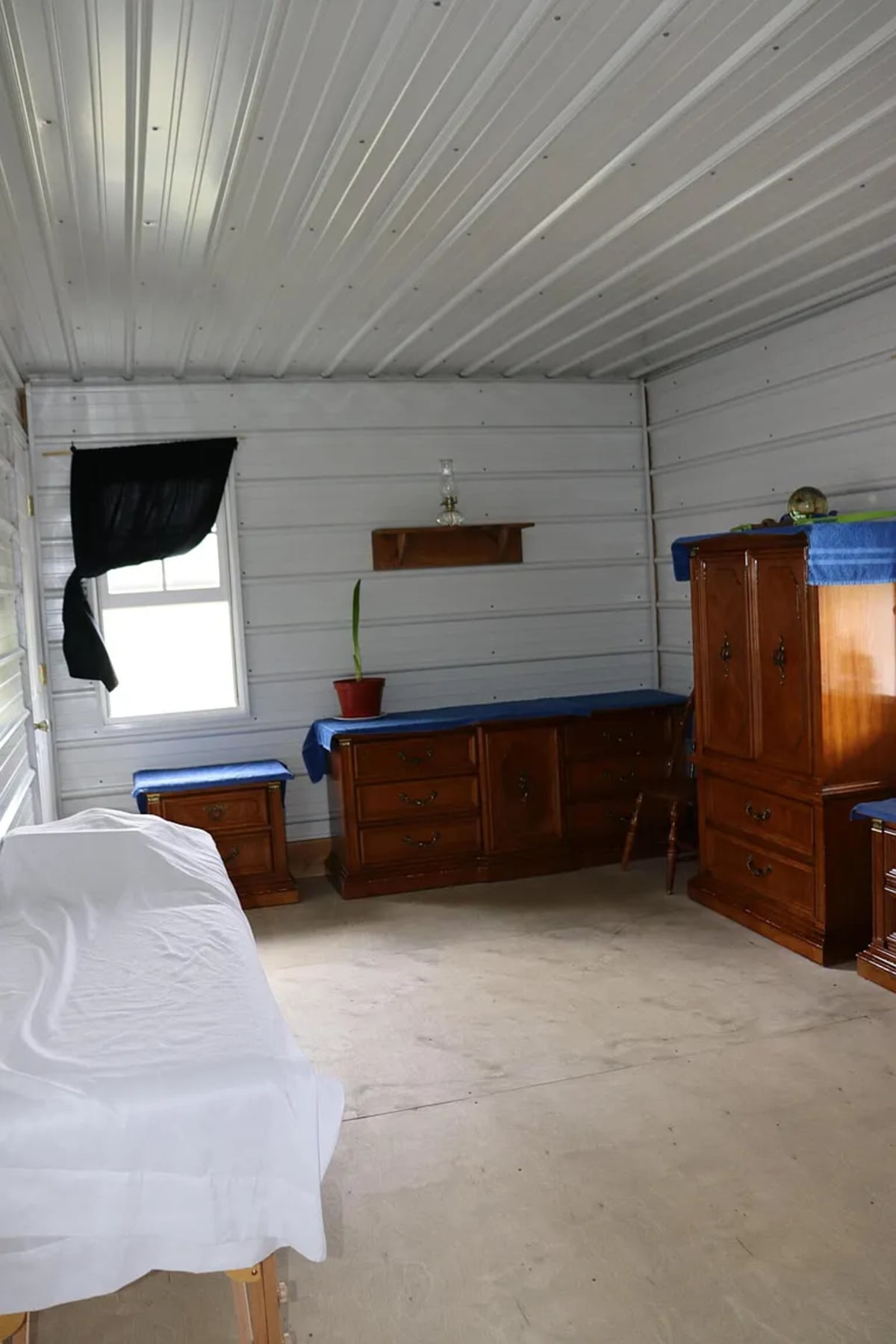 A plainer Amish bedroom with wooden dressers, an oil lamp on a shelf, and a black curtain