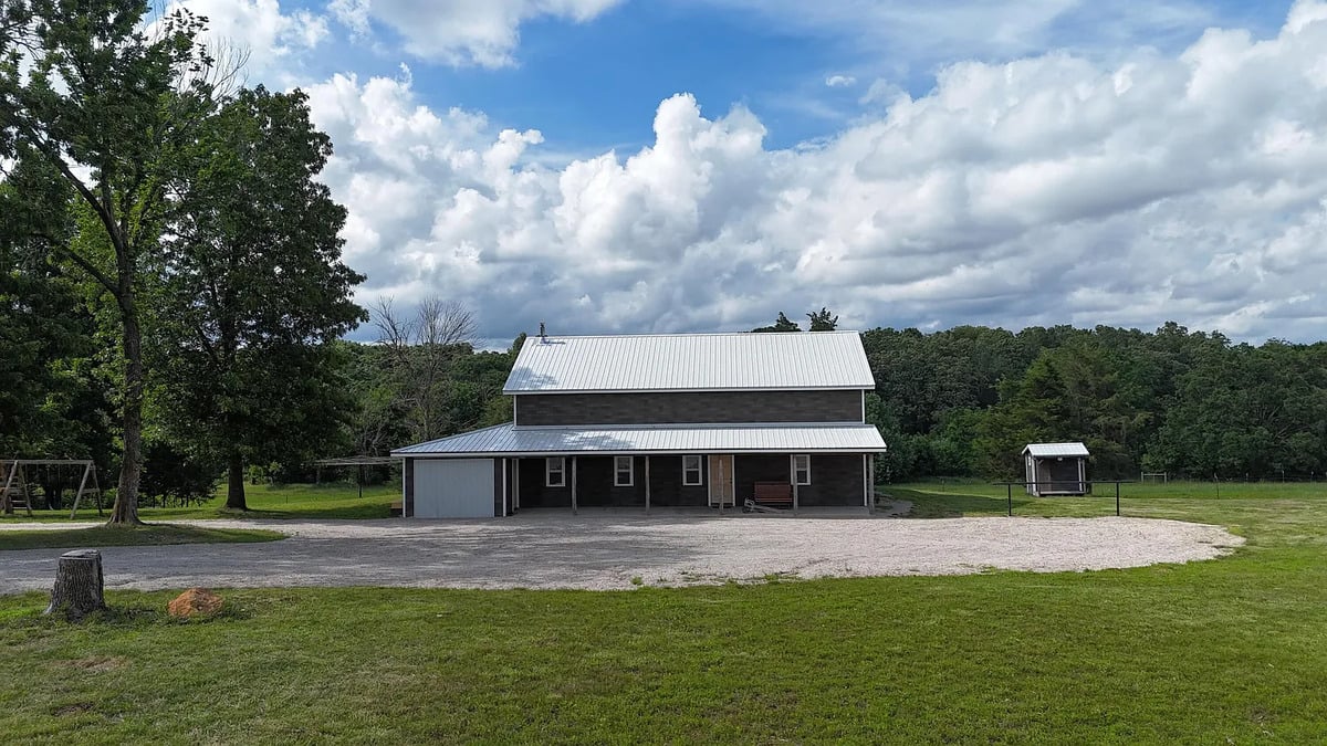Dark two-story Amish house with metal roof and covered front porch on a Missouri property