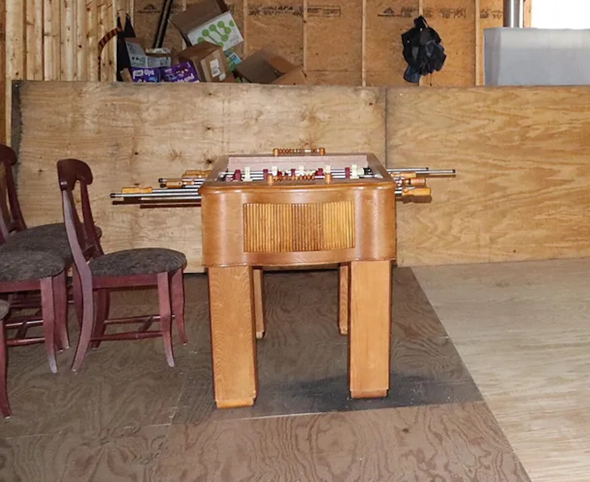 A wooden foosball table with chairs against a plywood wall in the unfinished upstairs