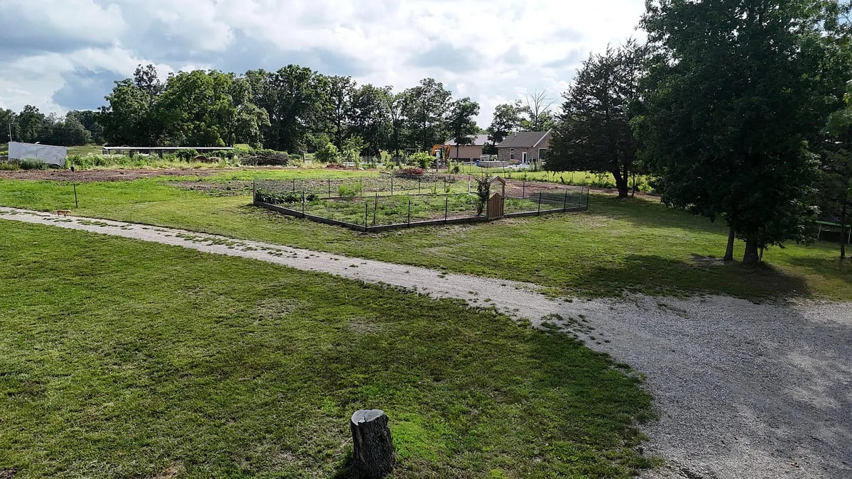 A fenced garden plot beside the Amish home with a neighboring property beyond